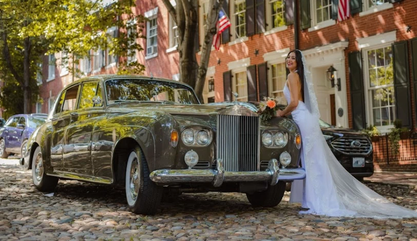 Portrait of a smiling bride leaning on a Rolls Royce Classic Car.